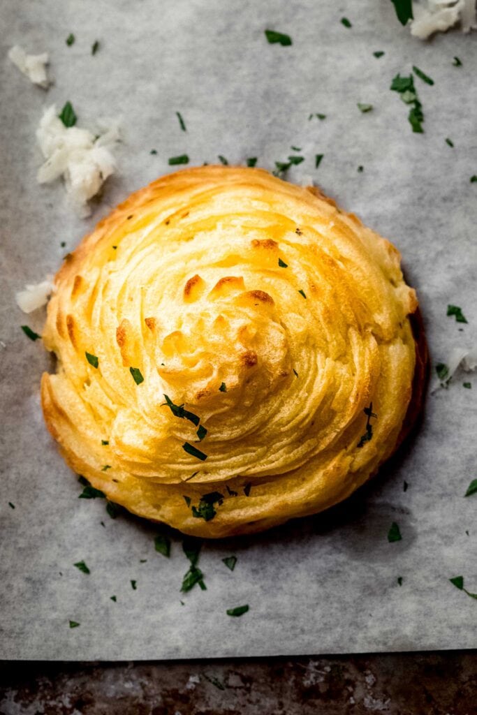 Single duchess potato on baking sheet with golden swirl.