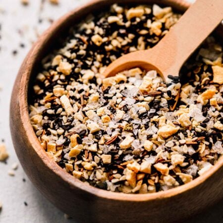 Close up of everything bagel seasoning in small bowl with wooden spoon.