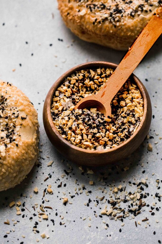 Bowl of seasoning next to bagels topped with spices.