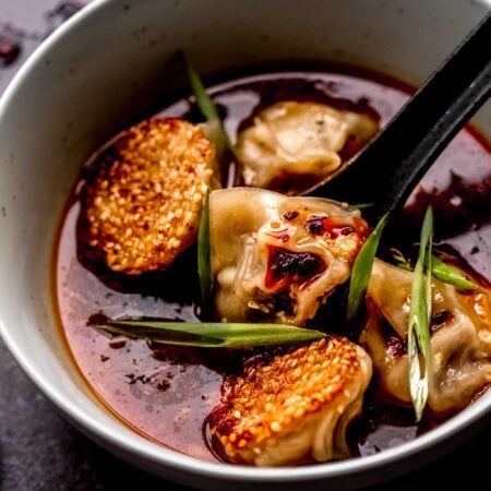 CLOSE UP OF BOWL OF LAMB DUMPLINGS IN SPICY GINGER BROTH.