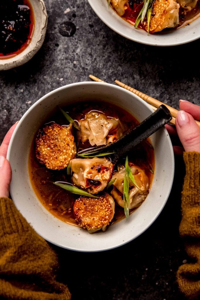 HANDS HOLDING BOWL OF LAMB WONTONS.