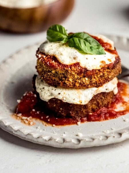 Eggplant parmesan stacked on plate and topped with basil leaves.