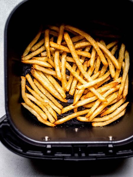 Cooked fries in air fryer basket.