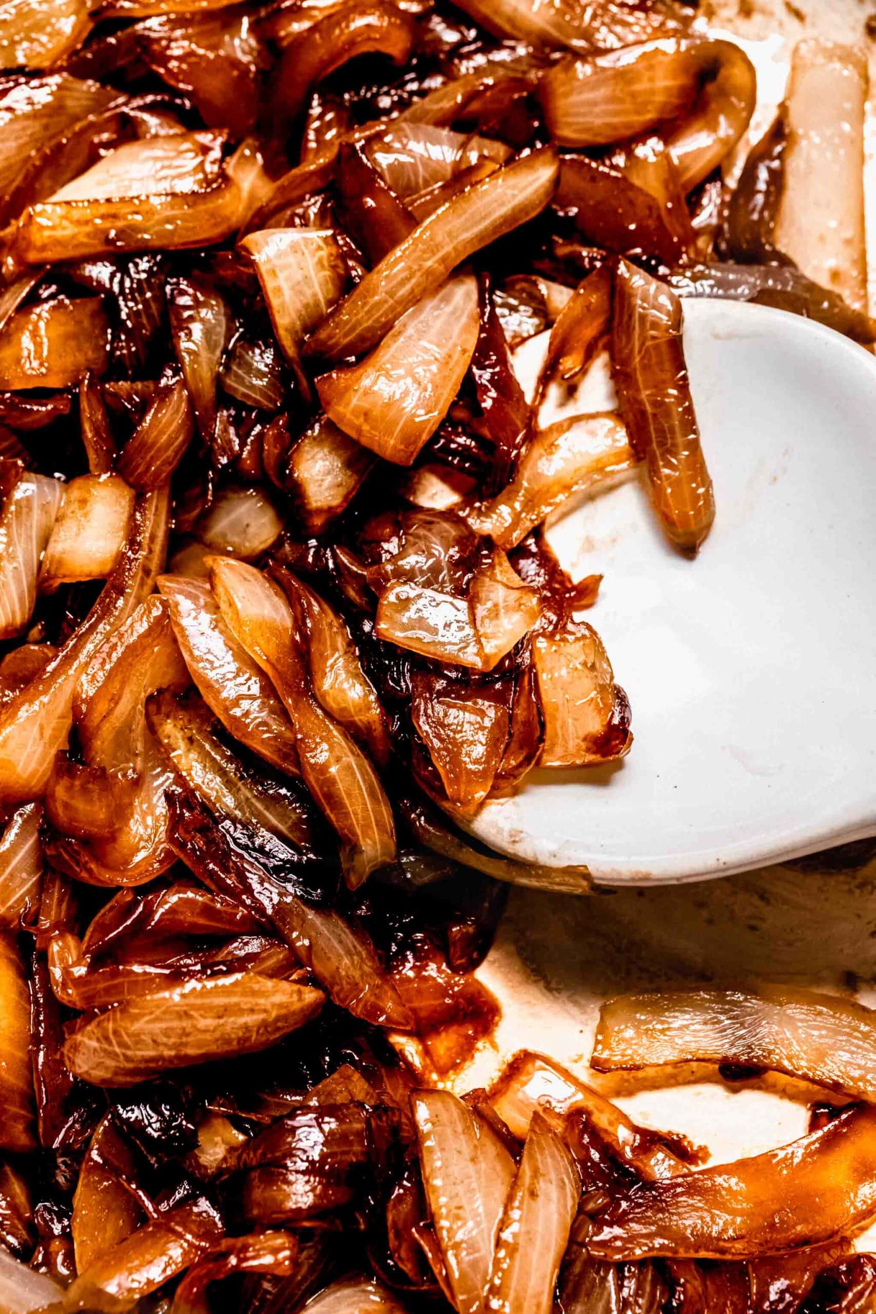 Large spoon digging into skillet of sauteed onions.