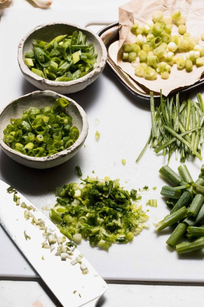 Green onions sliced 4 ways and laid out in small bowls next to knife.