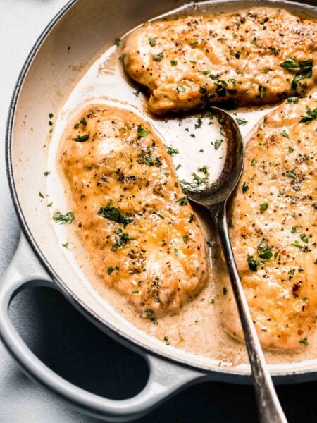 Chicken in white wine sauce in skillet with spoon and sprinkled with parsley.