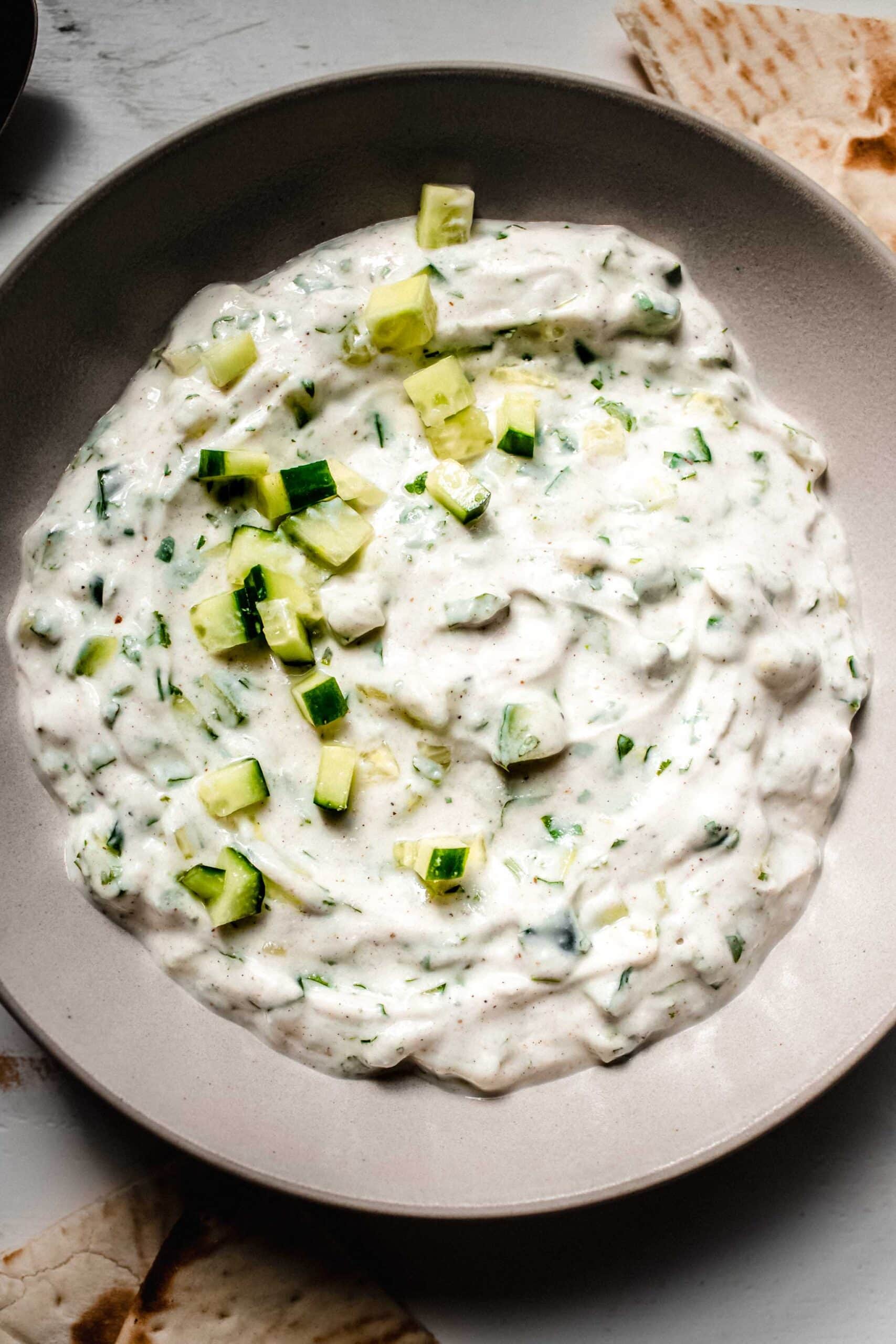 Overhead shot of prepared raita sauce in bowl next to pita pieces.