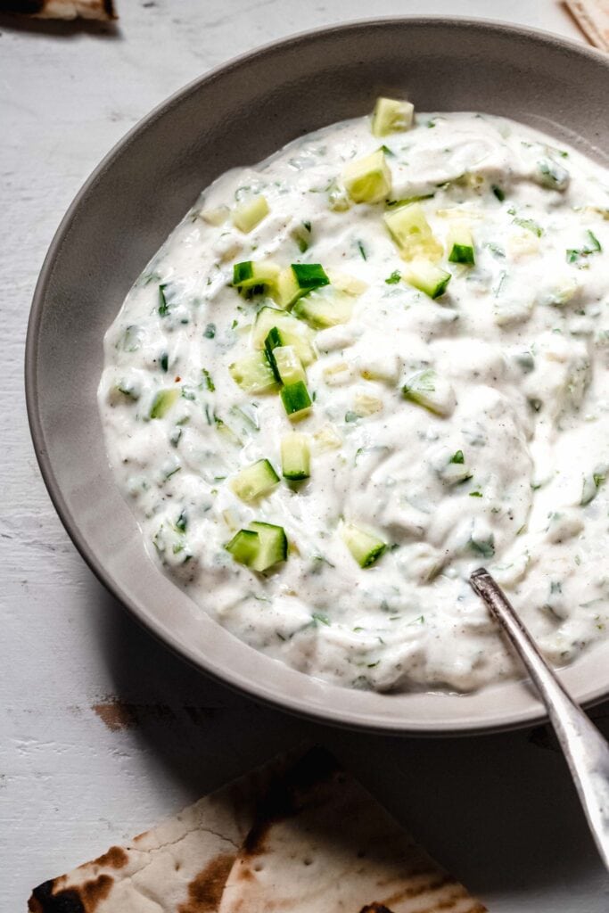 Side view of Raita sauce in bowl with serving spoon.