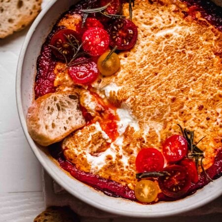 Baked goat cheese in white bowl with crostini being dipped in.