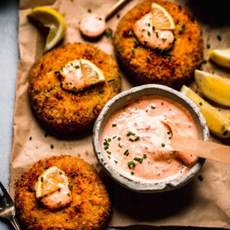 Crab cakes topped with lemon wedges and dollops of crab cake sauce.
