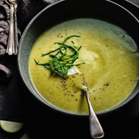 Side view of zucchini soup in grey bowl topped with sour cream and julienned zucchini.