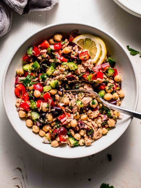 Tuna chickpea salad in bowl with lemon wedges and serving spoon.