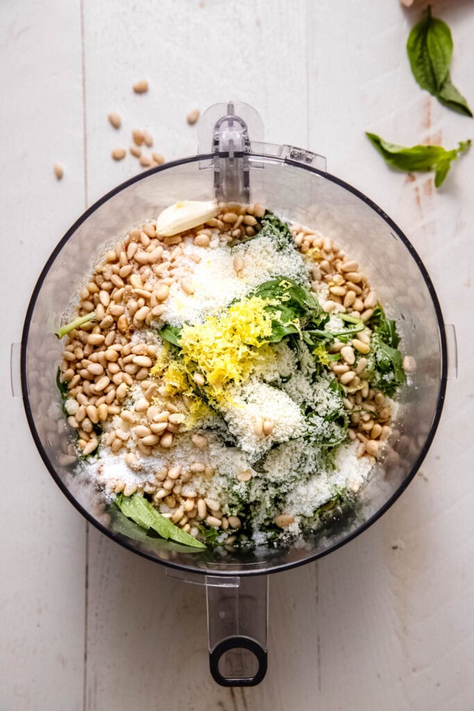 Ingredients for arugula pesto in food processor bowl.