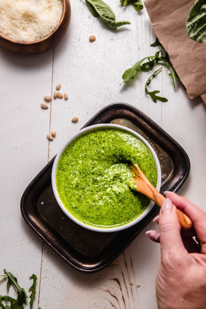 Spoon swirling in bowl of arugula pesto.