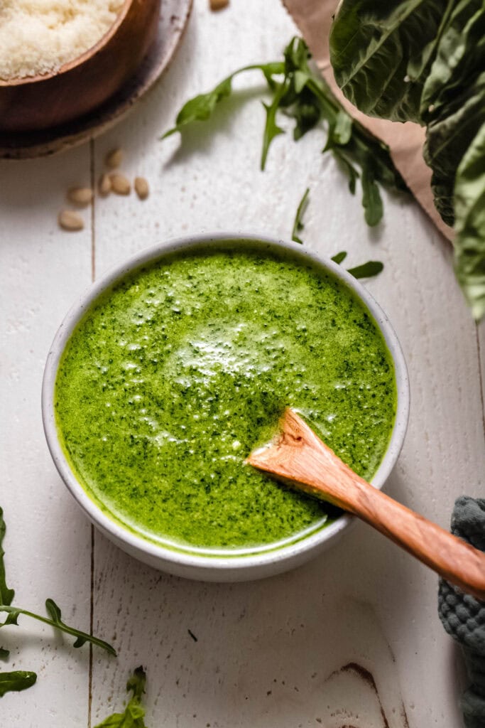 Side view of small wooden spoon in bowl of arugula pesto.