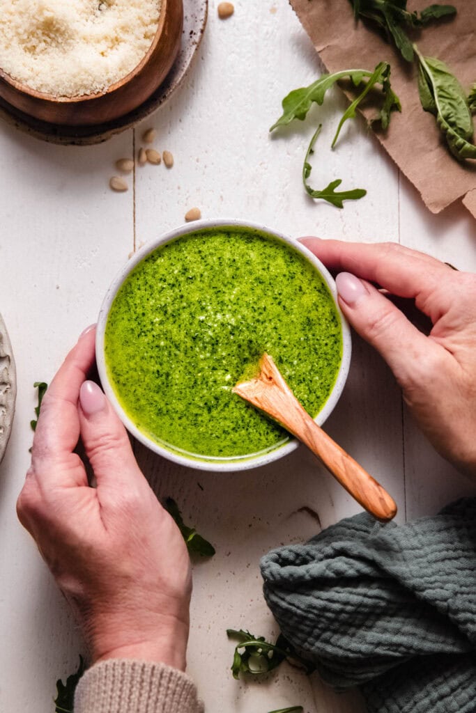 Hands holding bowl of arugula pesto.