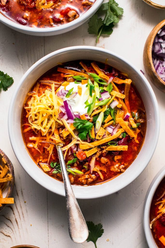 Overhead shot of instant pot chili in white bowl topped with sour cream and tortilla strips.