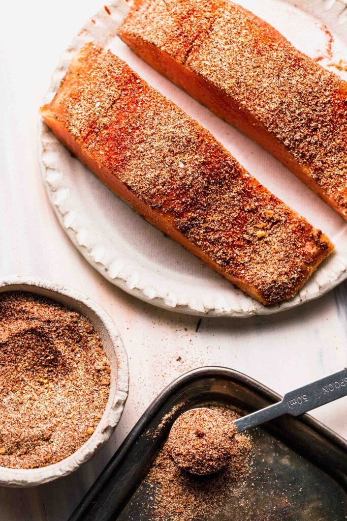Two uncooked salmon filets coated in dry rub.