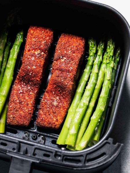 Salmon filets and asparagus in air fryer basket.