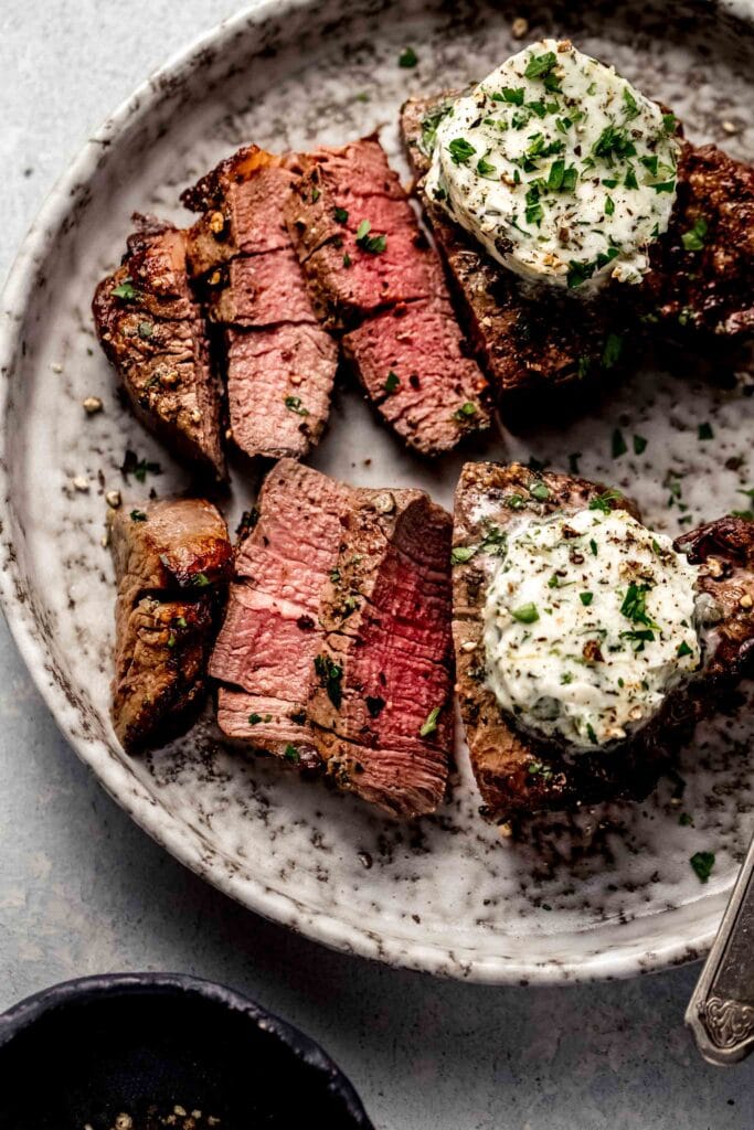 Two sliced air fryer filet mignons topped with garlic butter on plate.