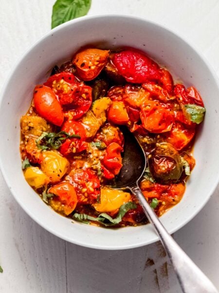 Air fried tomatoes in white bowl topped with basil sprigs.