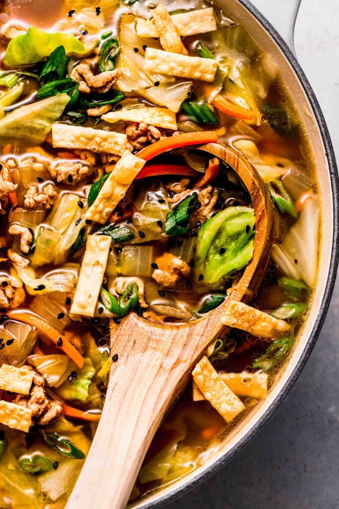 Close up of egg roll soup in pot with ladle.