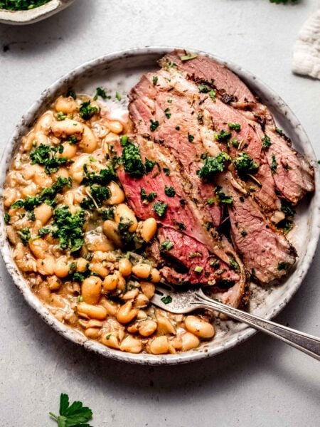 Sliced leg of lamb on plate with white beans and gremolata.