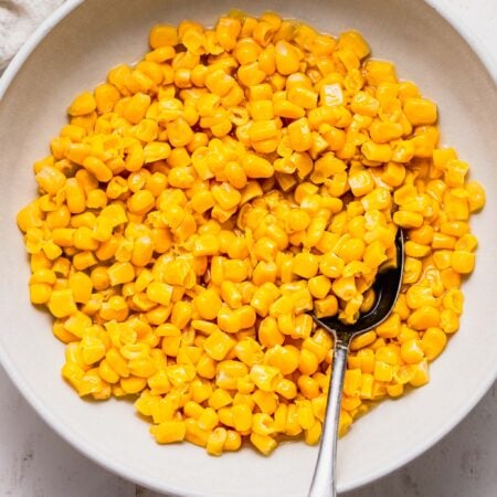 Cooked corn in white serving bowl with spoon.