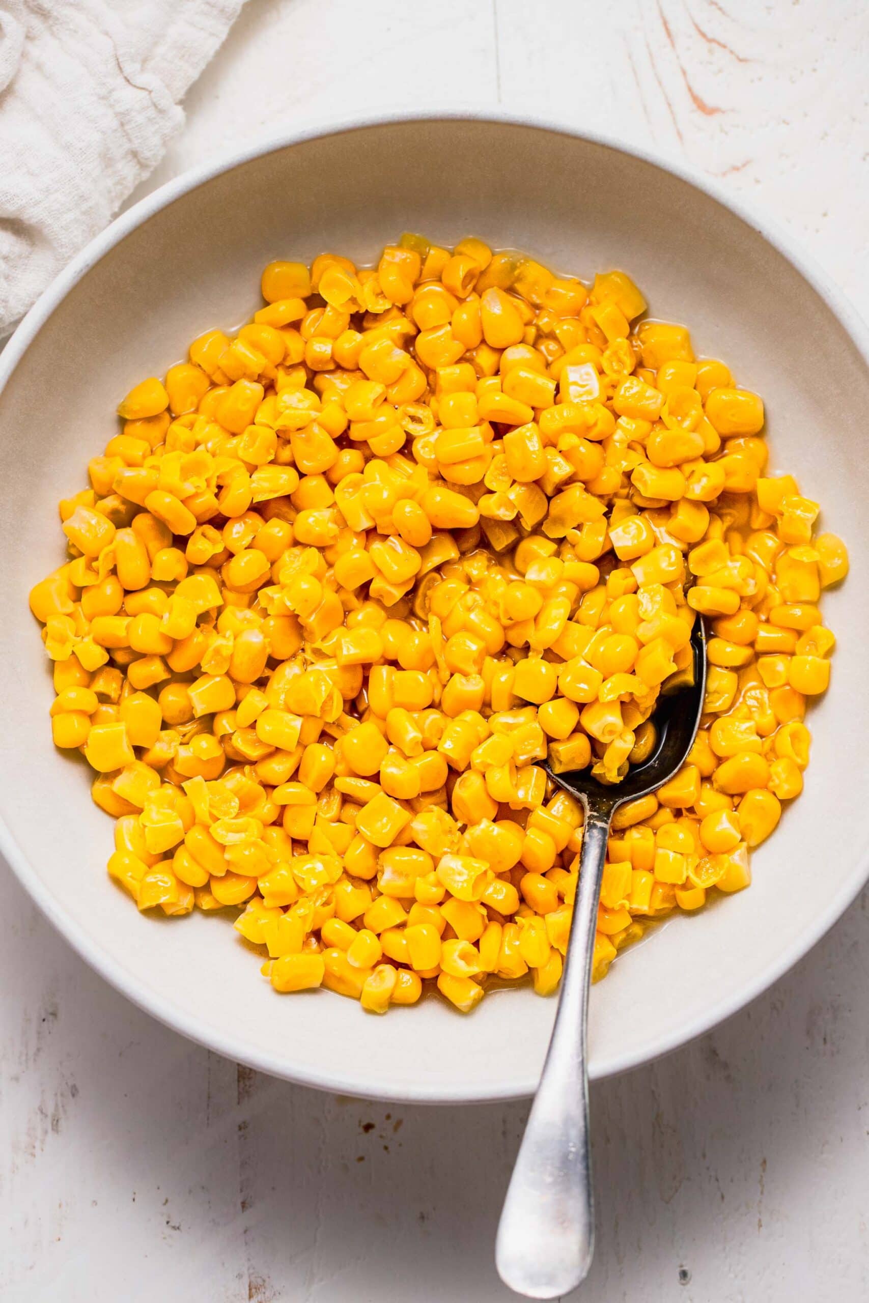 Cooked corn in white serving bowl with spoon.