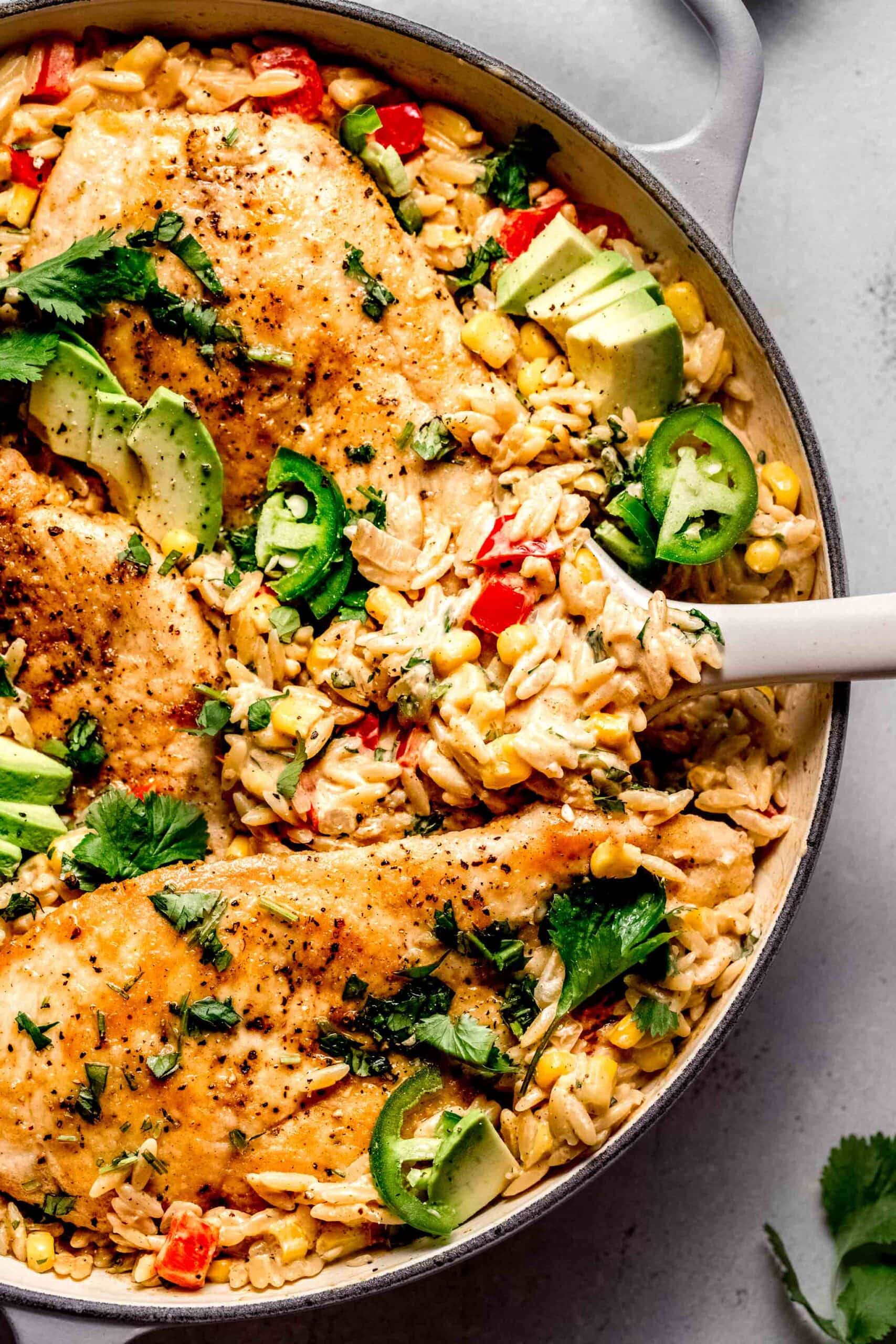 Cajun chicken orzo in skillet with serving spoon.