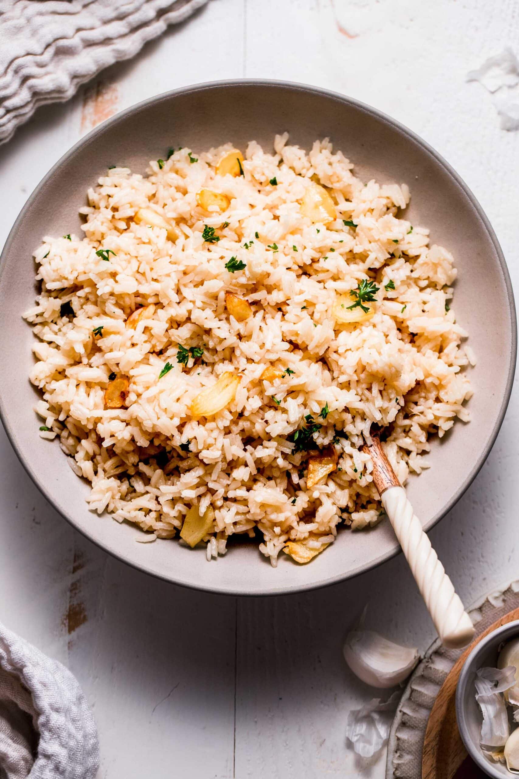 Garlic butter rice in white bowl with serving spoon.