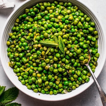 Simple minted peas in white serving bowl with spoon.