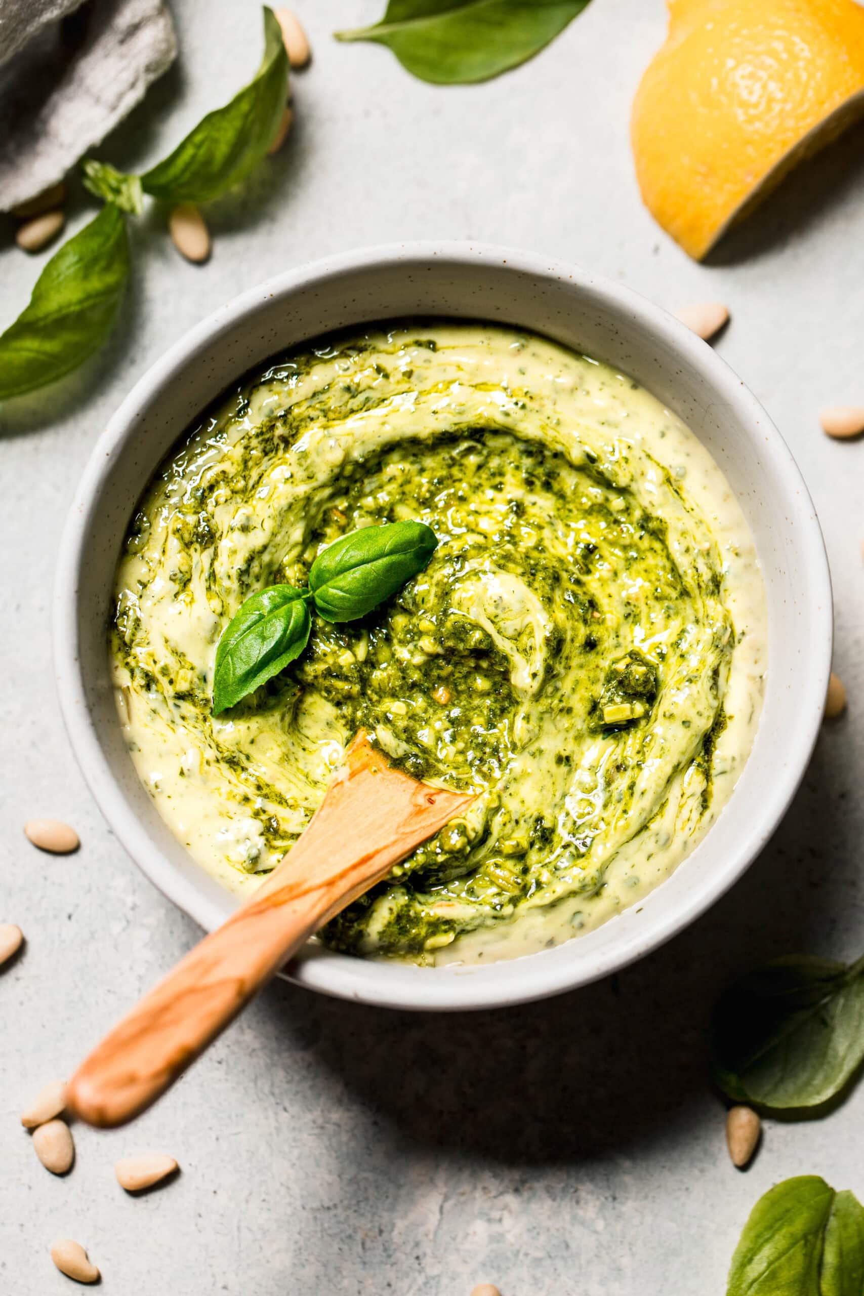 Homemade pesto mayo in bowl swirled with pesto and topped with basil leaf.