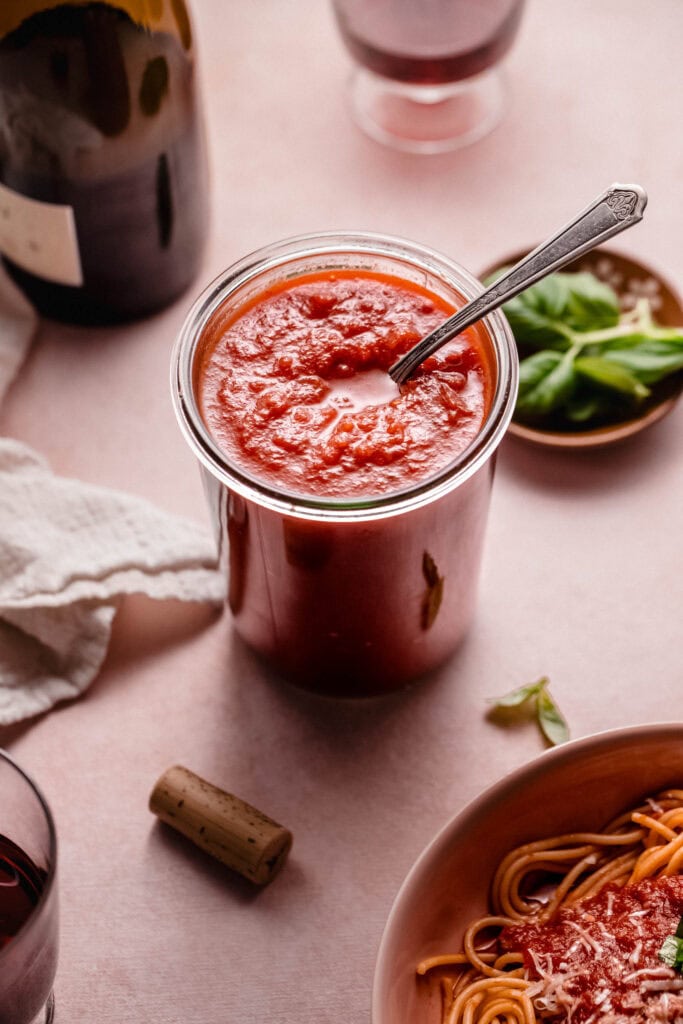 Red wine pasta sauce in jar on counter next to bottle of red wine.
