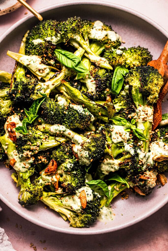 Overhead close up of bowl of roasted broccoli topped with basil tahini dressing.