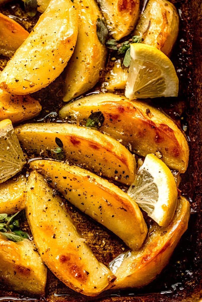 Close up of finished roasted potatoes on baking sheet sprinkled with lemon wedges and oregano.