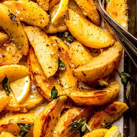 Greek roasted potatoes on baking sheet sprinkled with fresh oregano and lemon wedges.