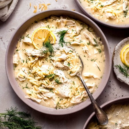 Overhead shot of bowl of greek avgolemono orzo soup on pink counter.