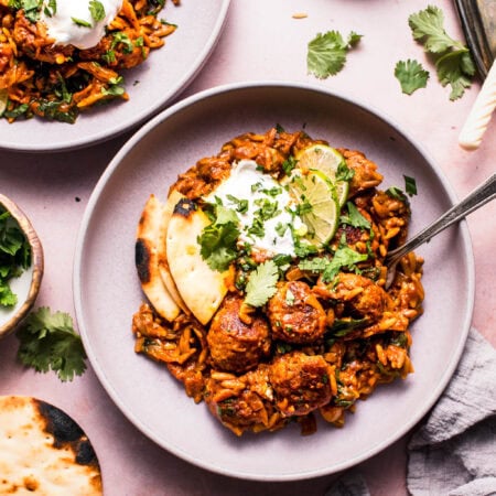 Two bowls of butter chicken meatballs over orzo ready to eat.