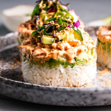Side view of layered tuna sushi stack on plate topped with furikake and seaweed.