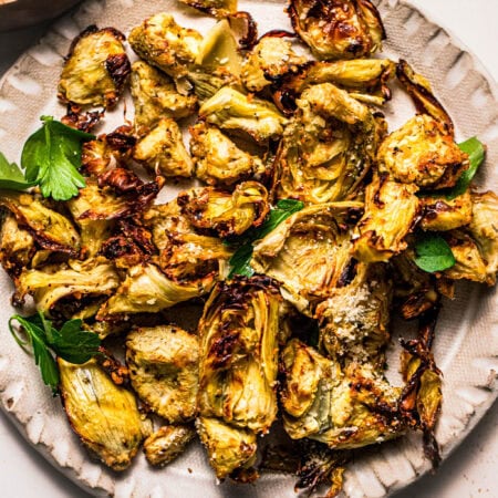 Air fried artichoke hearts on white plate with parsley leaves.