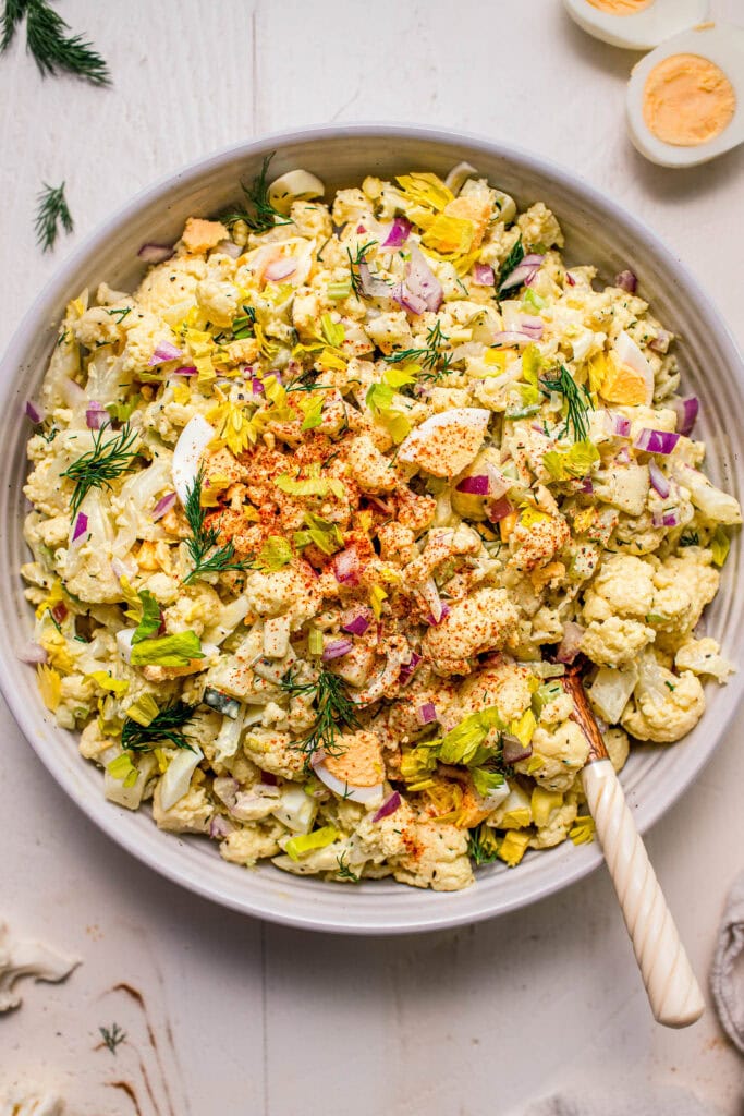 Prepared cauliflower potato salad in bowl with serving tongs.
