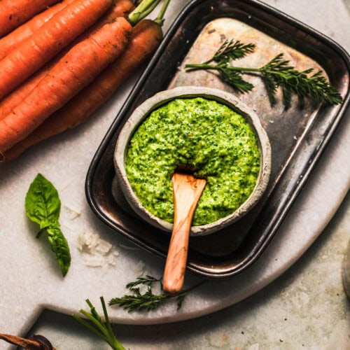 Side view of carrot top pesto on counter next to basil leaves and carrot tops.