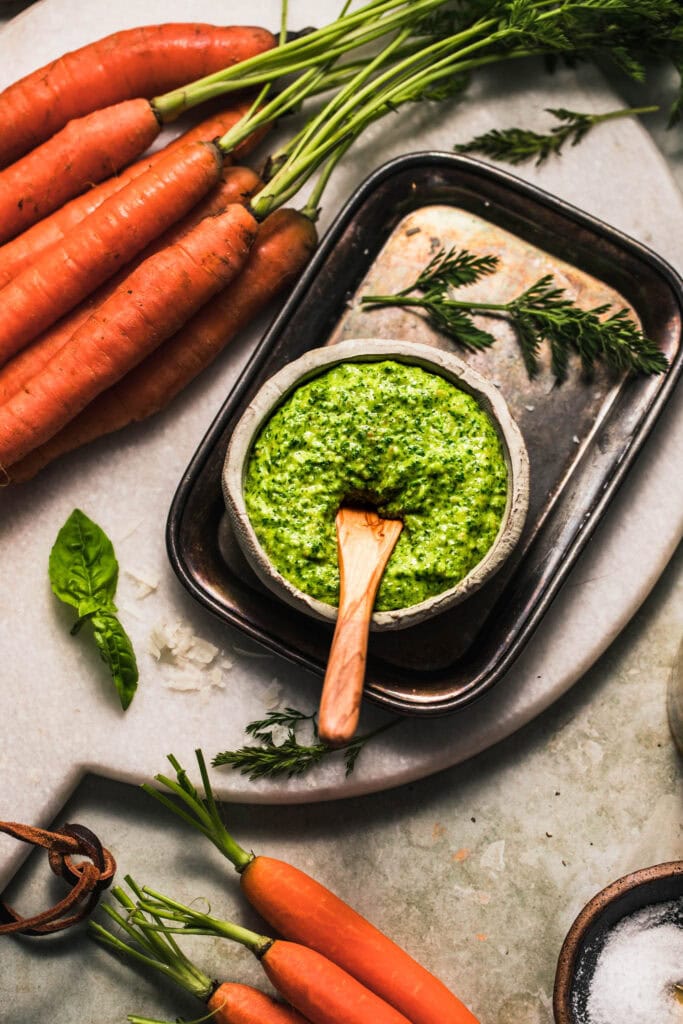 Side view of carrot top pesto on counter next to basil leaves and carrot tops.