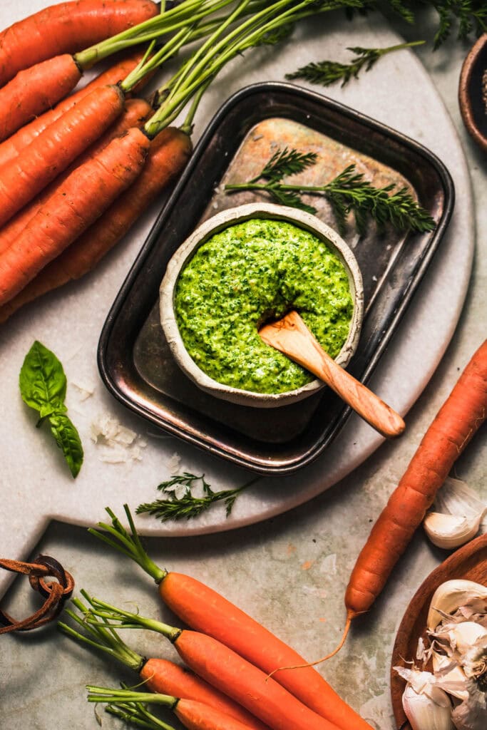 Bowl of carrot top pesto on counter next to carrots.