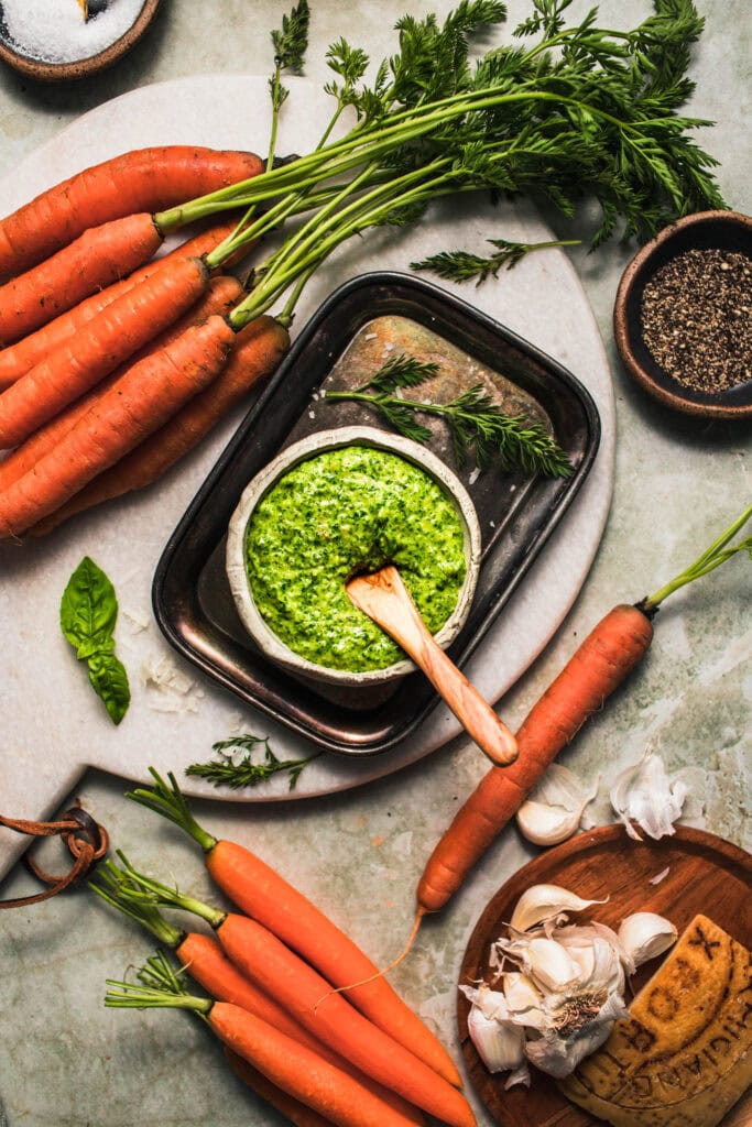 Bowl of carrot top pesto on counter next to carrots.