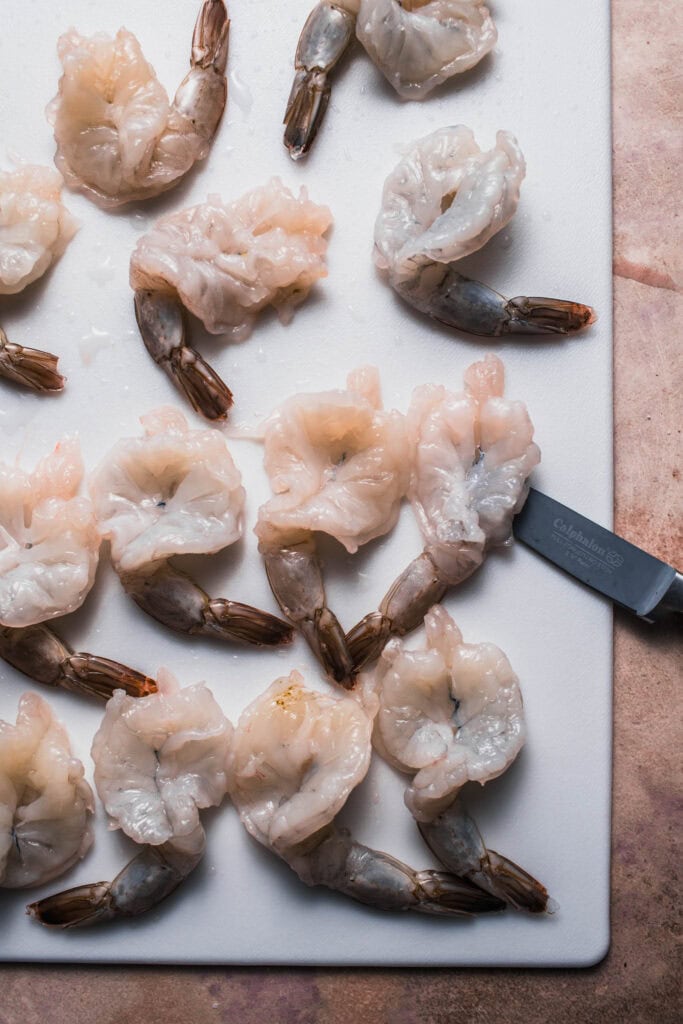 Shrimp being butterflied on cutting board.