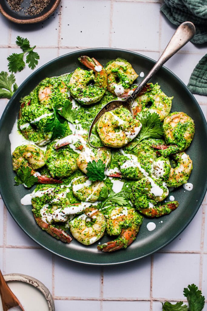 Green shrimp served on green plate with serving spoon.