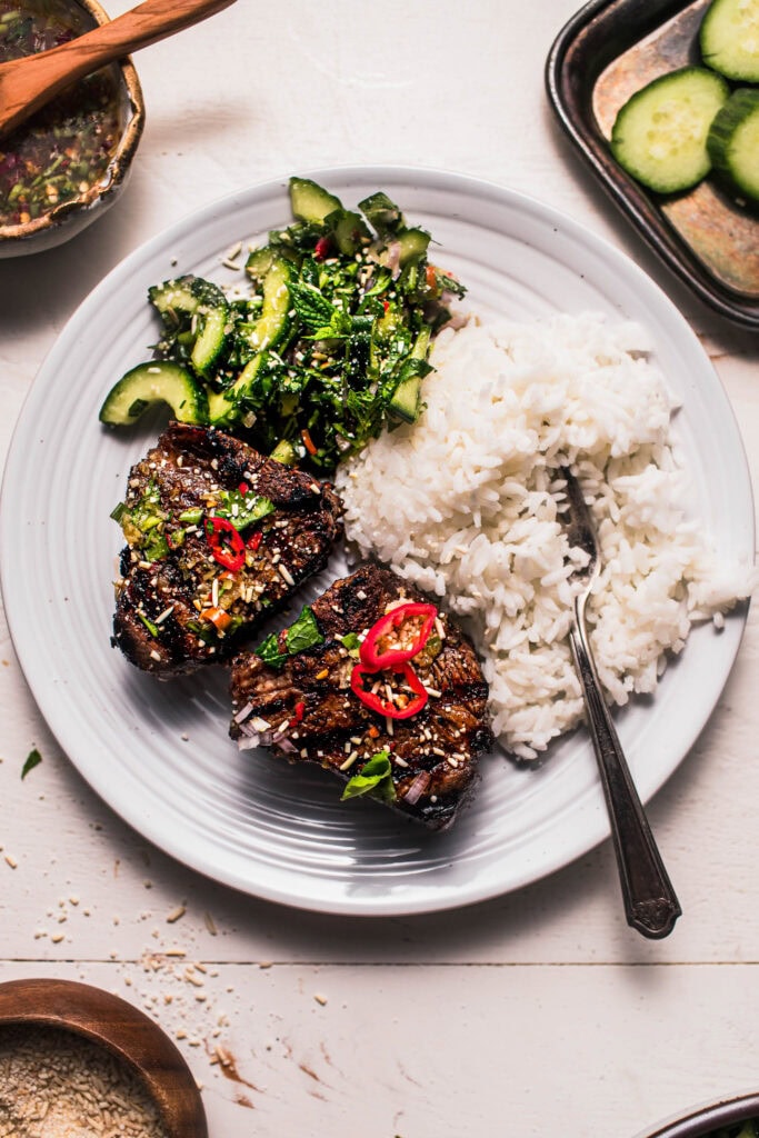 Grilled lamb chops on plate with rice and cucumber salad.