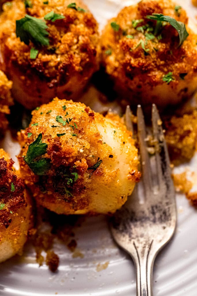 Close up of buttery panko topped scallops on plate with fork.